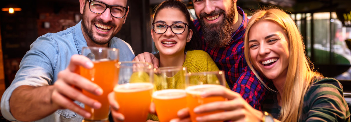 Eine Gruppe von Menschen stößt lachend mit Bier gefüllten Gläsern an