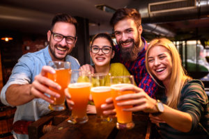 Eine Gruppe von Menschen stößt lachend mit Bier gefüllten Gläsern an